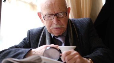 Yaşlı bir İtalyan beyefendi bir kafede oturuyor, bir sandalyede, kahve içiyor ve basını okuyor..
