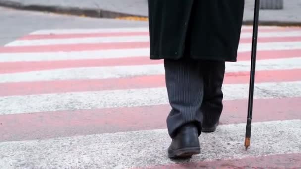 一个穿着旧鞋子 手里拿着棍子的老人急急忙忙地穿过人行横道 需要支助的人 — 图库视频影像
