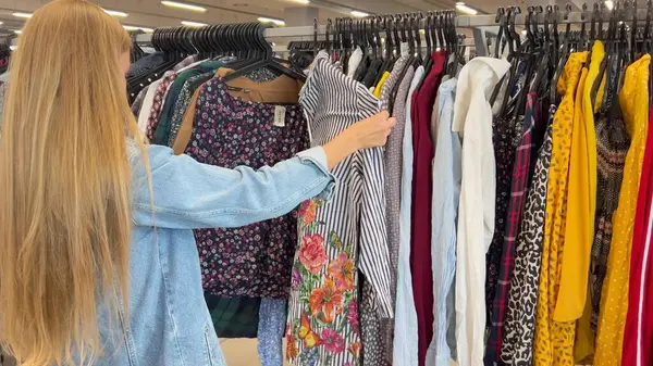 Used clothes, vintage fashion at a flea market. Side view of young woman shopping in thrift store. A customer in a vintage store