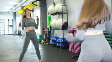 Genç bir kız spor salonunda aynanın önünde ısınma hareketleri yapıyor. Crossfit eğitimi.