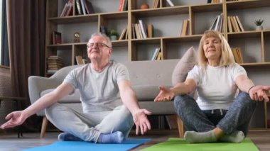 Spor, spor ve sağlık yaşam tarzı konsepti. Sakin, sağlıklı, kaygısız orta yaşlı çift 50 'li yaşlarda gözleri kapalı, evde meditasyon yapıyorlar..