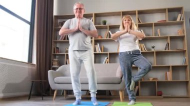 Güzel orta yaşlı çift mutlu bir şekilde gülümsüyor. Yüzümde bir gülümsemeyle ayakta dikilip, evde yoga yapıyorum. Sağlıklı yaşam biçimi. 