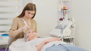 Bir güzellik uzmanı genç bir kadının yüzündeki deriyi muayene eder. Genç bir kız, kozmetoloji uzmanına yaptığı ziyarette profesyonel yardım alır..