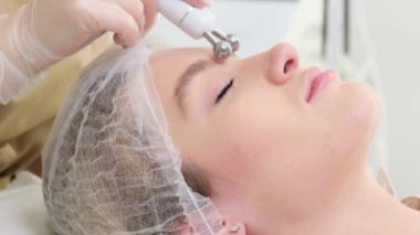 Yüz mikro akımı denilen uyarıcı bir yüz terapisi yapan bir güzellik uzmanının yakın çekimi. Bir kadının yüzünün estetik bakımı.