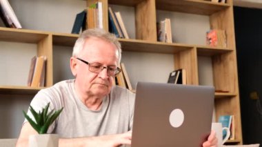 Orta yaşlı bir emekli evde oturuyor, dizüstü bilgisayar kullanıyor, e-postaları kontrol ediyor, kötü haberleri okuyor. Dedem laptopta vakit geçiriyor, başı ağrıyor..