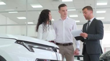 Otomobil işi, araba satışı, teknoloji ve insan konsepti - araba galerisinde veya galeride araba satıcısı olan mutlu çift.
