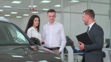 Araba galerisi. Otomobil galerisindeki müşterilere Neşeli Menajer Otomobil Gösteriyor. Satış müdürü genç bir çifte modern araba galerisinde yeni bir araba seçmeleri için yardım ediyor..