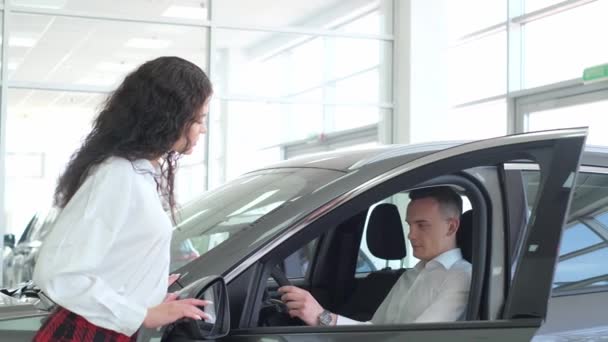 若いカップルがディーラーで新しい車を選ぶ クレジットで車を購入する — ストック動画