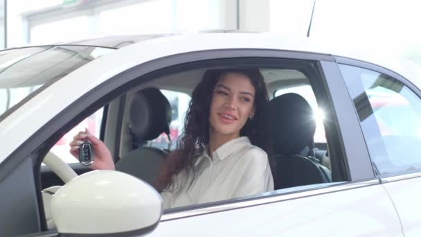 車のショールームで新しい高級電気自動車を運転する幸せな女性の肖像画 女性は新しい車の中で幸せの感情を示しています バイヤーは車を選択する — ストック動画