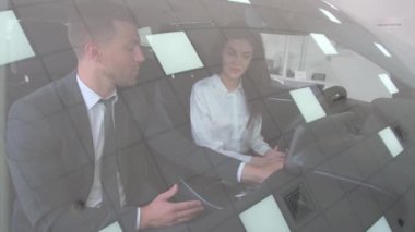 Esmer bir kadın araba galerisinde yeni bir arabanın sürücü koltuğunda oturuyor, direksiyonu tutuyor ve bir satış danışmanıyla konuşuyor. Otomobil işi, araba satışı..