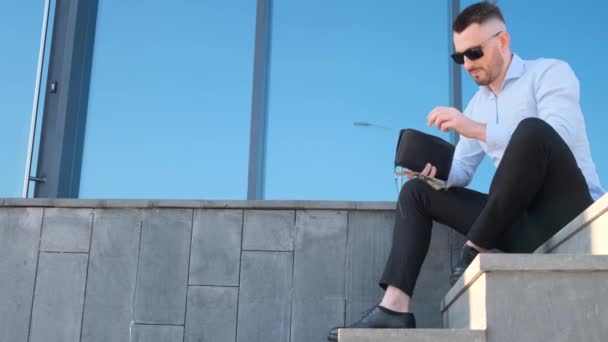 彼のオフィスセンターの近くに座っている間 彼の手に財布を持っている若いビジネスマン ビジネスコンセプト — ストック動画