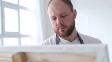 Modern bir resim yapmak için fırça kullanan, soyut bir tablo üzerinde çalışan bir sanatçının portresi.