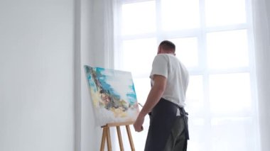 Bir sanatçı tuvale yağlı boya boyayla resim çizer. Bir sanatçı atölyedeki soyut bir yağlı boya resim üzerinde yaratıcı bir şekilde çalışır. Hobi konsepti.