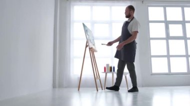 Modern bir resim yapmak için fırça kullanan, soyut bir tablo üzerinde çalışan bir sanatçının portresi.