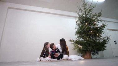 Anne ve çocuklar Noel tatili boyunca Noel ağacının yanında oynuyorlar. Mutlu bir aile..