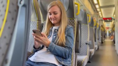 Avrupalı bir kadın akıllı telefon uygulaması kullanarak tren koltuğunda dinleniyor. Cep telefonundaki mesajları kontrol ediyor. Seyahat kavramı.