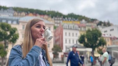 Güzel bir kadın Karlovy Vary 'deki bir kaynaktan maden suyu içiyor. Çek Cumhuriyeti 'nde turizm kavramı.