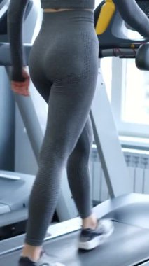 Dikey video, seksi kız spor salonundaki koşu bandında kardiyo çalışması yapıyor. Aktif yaşam tarzı, spor konsepti. Dikey video.