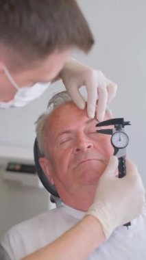 Bir estetik cerrahın göz bölgesindeki sarkık deriyi inceleyip kalibre ile ölçtüğü dikey video. Estetik cerraha danışmanlık. 