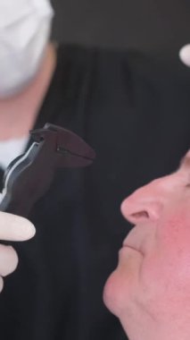 Estetik cerraha danışmanlık. Yaşlı bir adamın yüzünde ameliyat için hazırlıklar yapılıyor. Plastik metodla yüzün gençleştirilmesi. Dikey video.