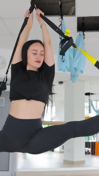 一个漂亮的女孩在吊床上做反重力飞行瑜伽练习 年轻而灵活的女子在健身俱乐部的空中伸展秋千练习 垂直录像 — 图库视频影像