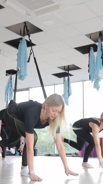 女子团体在空中伸展秋千练习 空中飞行瑜伽练习在健身俱乐部的吊床上进行 垂直录像 — 图库视频影像