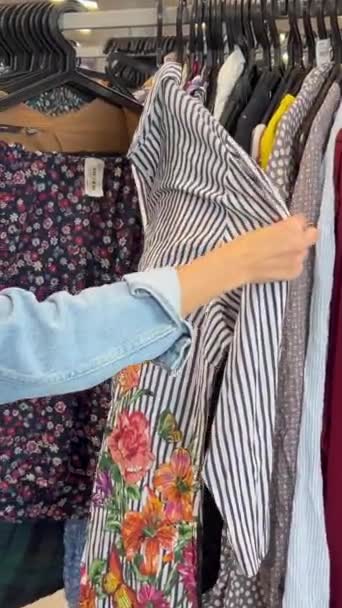 フリーマーケットで使用された服 ヴィンテージファッション 流通店で買い物をする若い女性の側面 ヴィンテージショップのお客さん バーティカルビデオ — ストック動画