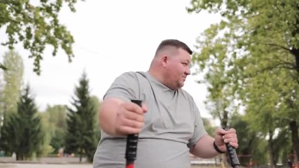 年轻的胖子在公园里的练习机上跑着 喘息着 可持续的动力 肥胖的问题 体重减轻 — 图库视频影像