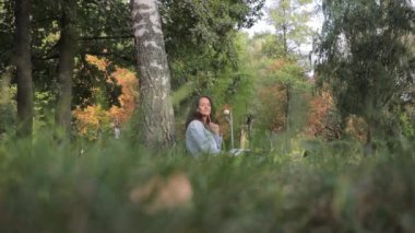 Güzel bir öğrenci kız çocuğu parktaki bir ağacın altında bilgisayarla oturuyor. Eğitim kavramı ve uzak çalışma.