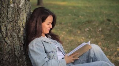 Akşam güneşinde piknik sırasında ağacın altında kitap okuyan genç bir kadın. Park yerinde kitap okuyan, üniversite veya üniversite sınavlarına hazırlanan genç bir kadın..