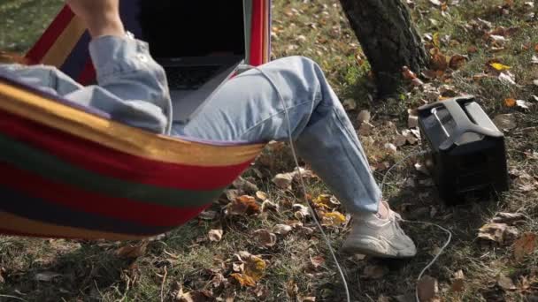 소녀는 충전소에서 충전하는 노트북을 사용하고 있습니다 공원에서 해먹에 — 비디오