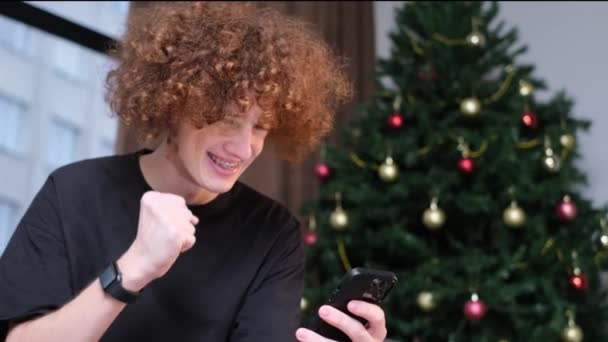 Weihnachtsgewinn Mann Mit Handy Der Nähe Von Buntem Winterbaum Zimmer — Stockvideo