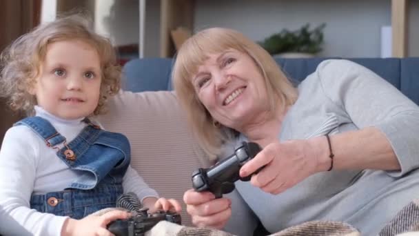 快乐的中年奶奶和小孙女坐在沙发上玩电脑游戏 快乐的老奶奶和小孙子玩得很开心 — 图库视频影像