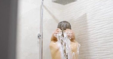 Genç bir kadın saçını yıkıyor ve duş alıyor. Saç bakımı. Güzel genç bir kadın duş alıyor ve saçını şampuanlıyor, sağlık hizmetleri konsepti..