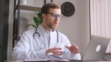 Modern bir klinikte beyaz önlüklü bir doktor oturmuş bilgisayarla görüntülü konuşma yapıyor, danışmanlık yapıyor..