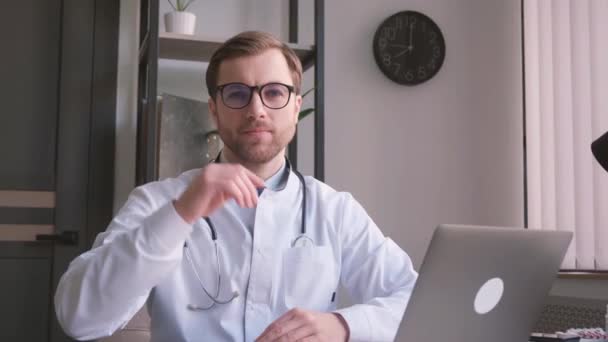 若い医師が眼鏡を外してカメラを見る オフィスで働いている間医者 — ストック動画