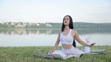 Spor giyimli genç bir kadın şehir parkında bacaklarını açıyor. Sağlık, yaz, spor. Genç zayıf kadın göl kenarında dinlenme egzersizleri yapıyor..