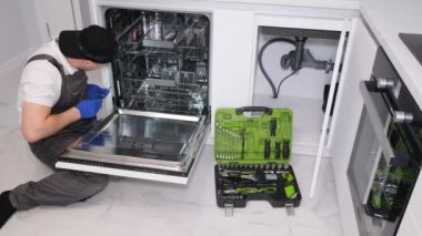 Bir adam mutfak odasına yeni bir bulaşık makinesi yerleştiriyor..