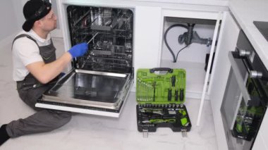 Genç bir erkek tesisatçı bulaşıkçıyı tamir ediyor..