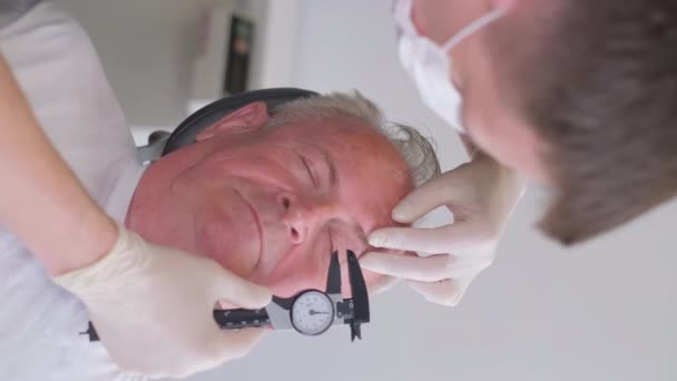 プラスチック外科医の垂直ビデオは 目の領域のサギの皮膚を検査し キャリパーでそれを測定します プラスチック外科医の相談 — ストック動画