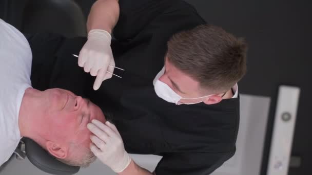 在手术室里 一位整形外科医生在动手术前检查了一位老人的脸 整形外科医生会诊 防止老化 垂直录像 — 图库视频影像