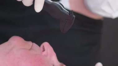 Estetik cerraha danışmanlık. Yaşlı bir adamın yüzünde ameliyat için hazırlıklar yapılıyor. Plastik metodla yüzün gençleştirilmesi. Dikey video.