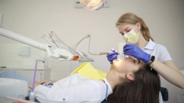 Dişçi muayenehanesinde diş tedavisi gören güzel bir kadın hasta. Kadın dişçi. Bir dişçi, dişçi koltuğunda yatan bir kızın dişlerini tedavi eder..