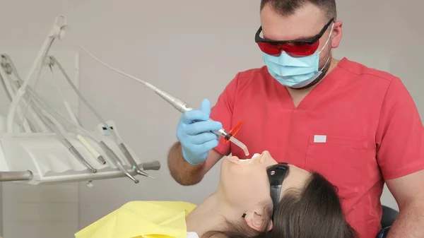 Dentist with patient in dental chair providing manipulations in oral cavity. Practitioner male dentist drilling tooth to female patient in dental studio