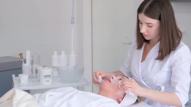一位皮肤科医生在给一位年轻女性做美容治疗前 用矿泉中的海藻酸钠面膜清洁她的脖子和脸 — 图库视频影像