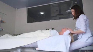 Profesyonel bir kozmetikçi, cilt bakımı sırasında yüz derisini nemlendirici bir maskeyle kaplar..