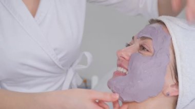 Bir kozmetik uzmanı bir kadının yüzüne kozmetik maske takar. Kadınların yüzü aljinat bir maskeyle kaplıdır. Bir kadının yüzünde kozmetik prosedür.