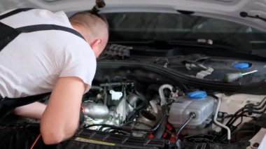 Otomobil tamirhanesi. Tamirci araba motorunu inceliyor. Tamirci araba motoruna bakıyor ve lambayı tutuyor.