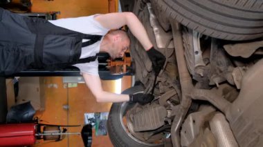 Dikey video, arabada yağ değişimi. Araba servisinde çalışırken oto tamircisi.