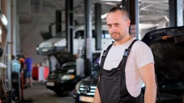 Otomobil tamircisinin atölyede ayakta dikilirken başparmaklarını gösteren portresi.